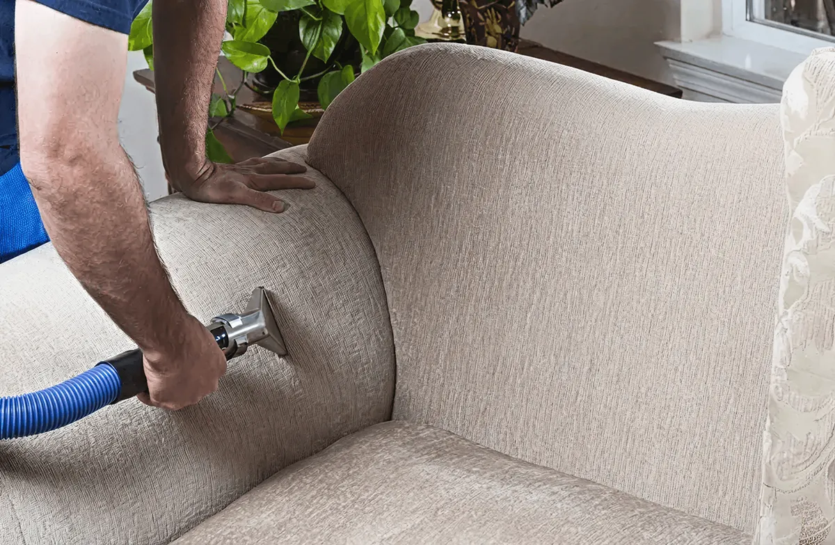 Professional upholstery cleaner deep-cleaning a fabric sofa with a handheld extraction tool and hose, Boston, MA.